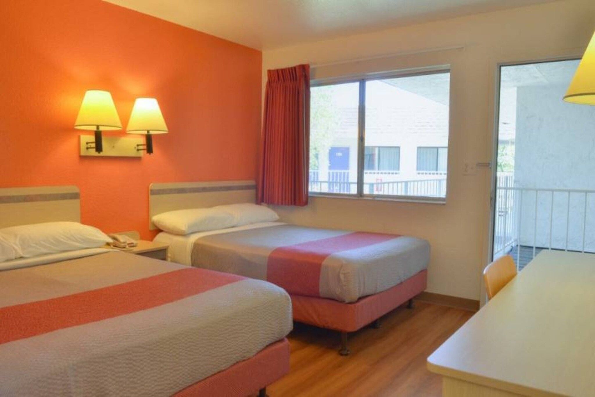 A hotel room with two beds, a desk, and a window with curtains.