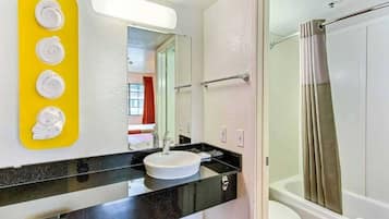 A bathroom with a black countertop, a white sink, a mirror, and a shower area.