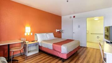 Quarto de hotel com cama, escrivaninha, cadeira, televisão e porta que dá para outro cômodo.