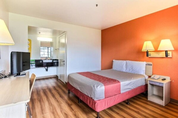 A hotel room with a bed, bedside table, lamp, and a desk with a chair.