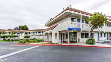 Um motel de dois andares com um letreiro de 'welcome', área de estacionamento coberta e céu claro.