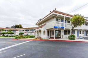Um motel de dois andares com um letreiro de 'welcome', área de estacionamento coberta e céu claro.