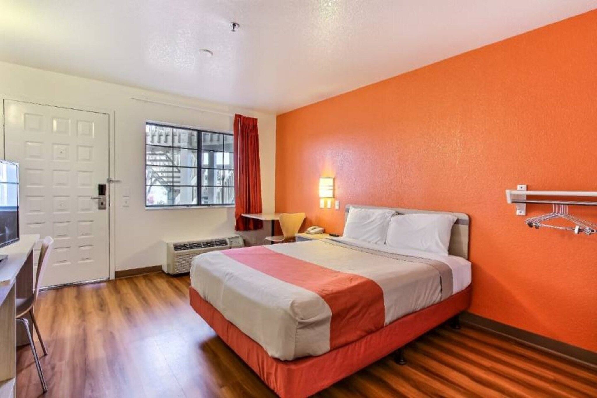 Een hotelkamer met een bed, een bureau, een stoel, een raam met gordijnen en een wandlamp.