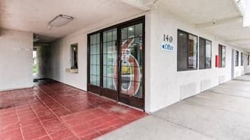 Entrada de um edifício com porta de vidro, placa indicando 'Office 140' e piso ladrilhado em vermelho.