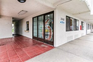 Entrada de um edifício com porta de vidro, placa indicando 'Office 140' e piso ladrilhado em vermelho.