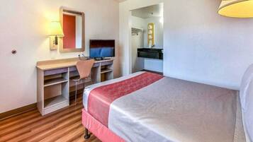 A hotel room with a bed, a desk with a chair, a television, and a mirror.