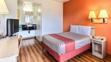 Quarto de hotel com cama, mesa de cabeceira, luminária e escrivaninha com cadeira.