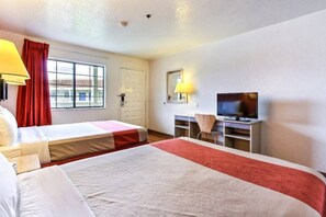 A hotel room with two beds, a television, a desk, and a window with curtains.