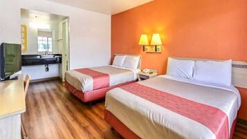 Habitación de hotel con dos camas, un escritorio, un televisor y un baño visible a través de una puerta abierta.