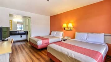 Quarto de hotel com duas camas, uma escrivaninha, uma cadeira, televisão e banheiro visível por uma porta aberta.