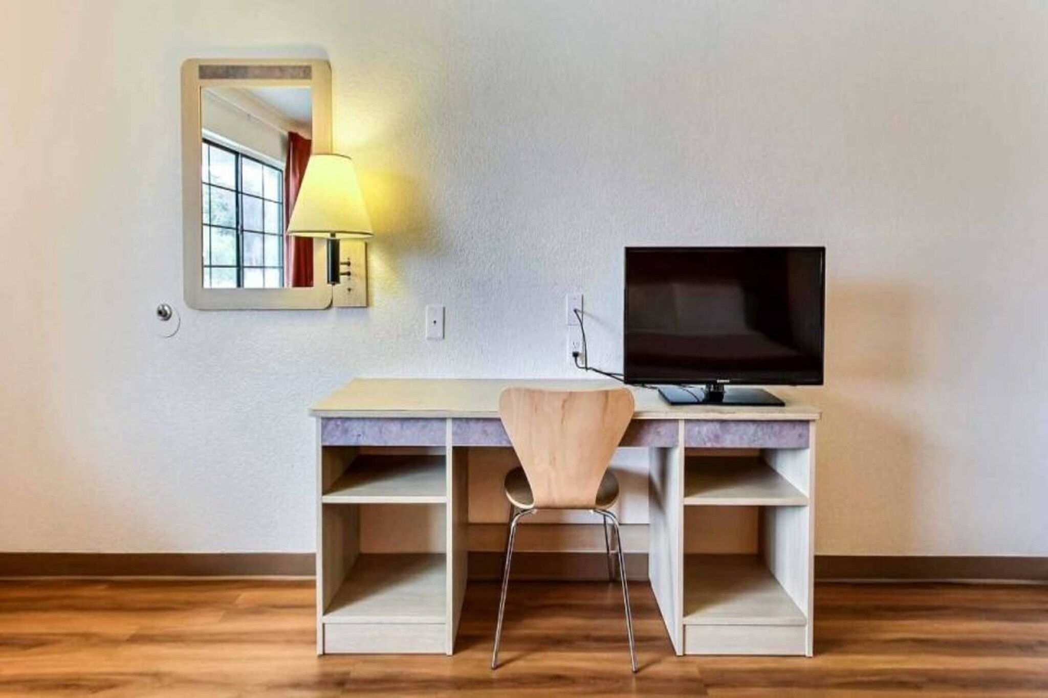 A room with a desk, chair, TV, and a lamp.