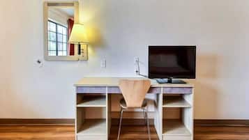 A room with a desk, chair, TV, and a lamp.