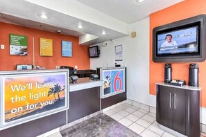 Uma área de recepção de hotel com balcão, televisão na parede e diversos avisos e cartazes.