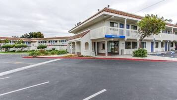 Um motel com uma placa de 'Welcome', estacionamento e um edifício com telhado de telhas vermelhas.