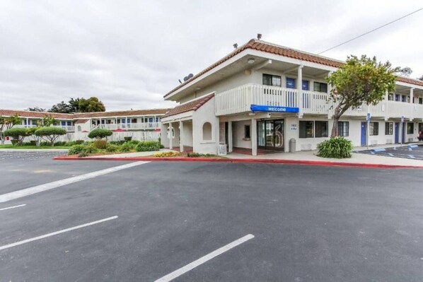 A motel with a 'Welcome' sign, a parking lot, and a building with a red-tiled roof.
