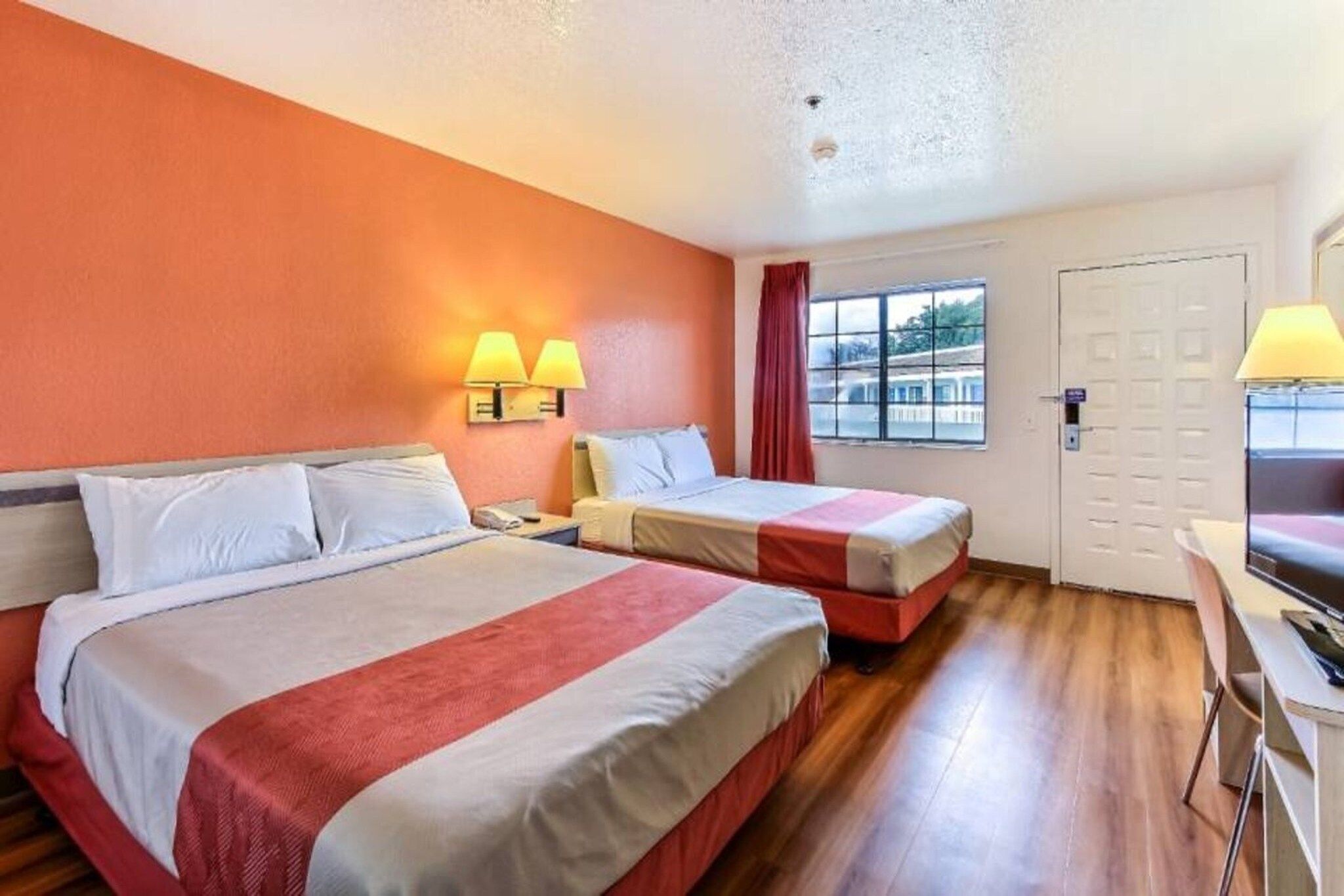 Een hotelkamer met twee bedden, een bureau, een stoel, een raam met uitzicht en een deur.