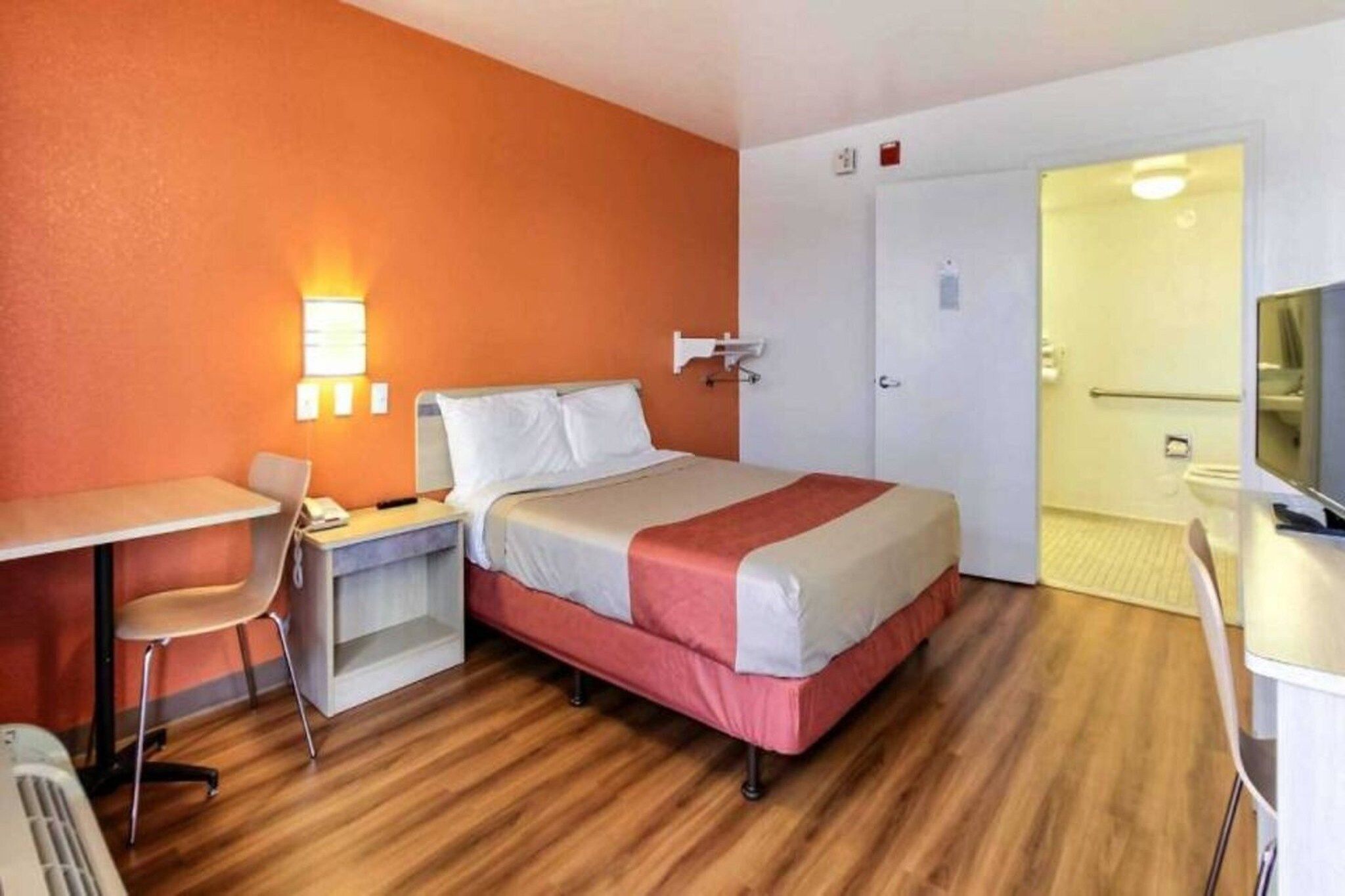 A hotel room with a bed, desk, chair, and a television.