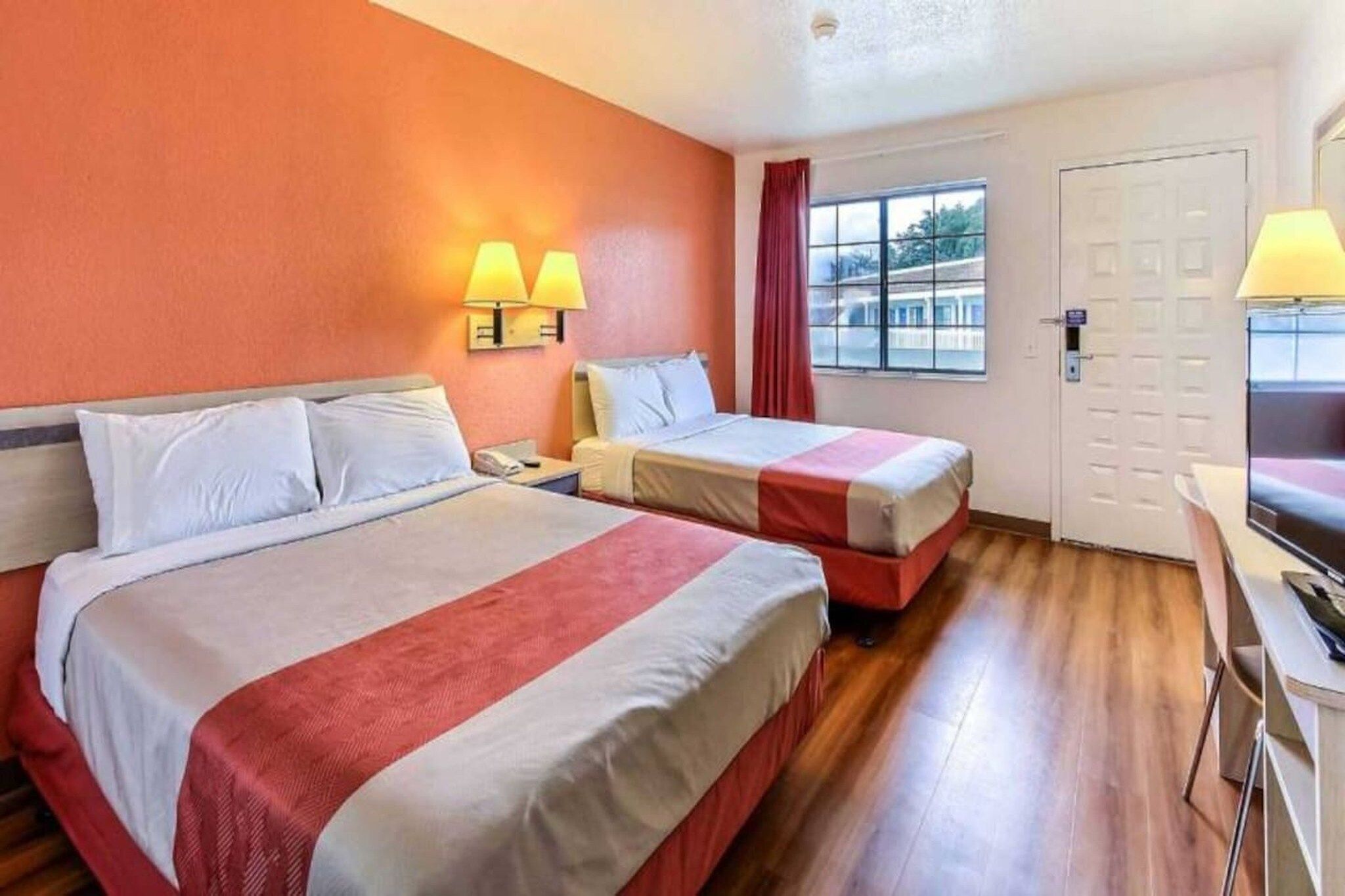 Une chambre d’hôtel avec deux lits, un bureau et une fenêtre avec des rideaux.