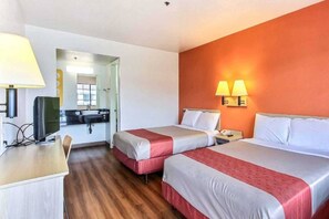 Habitación de hotel con dos camas, un escritorio, una silla, un televisor y un baño visible a través de una puerta abierta.