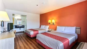 Quarto de hotel com duas camas, uma escrivaninha, uma cadeira, uma televisão e um banheiro visível por uma porta aberta.