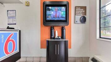 Um saguão de hotel com uma televisão fixada na parede, uma placa indicando cobrança matinal gratuita e uma placa com o número 6 Motel.