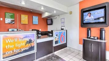 A hotel reception area with a counter, a television mounted on the wall, and various signs and posters on the walls.