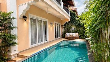 A swimming pool with a tiled edge, a covered balcony with a railing, and a view of a bamboo fence.