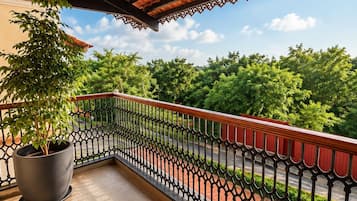 A balcony with a potted plant, a patterned railing, and a view of greenery.