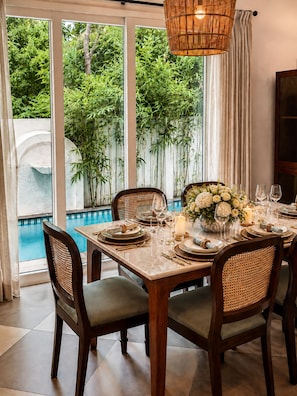 A dining area with a pool view, a table set for four, and a hanging light fixture.