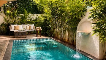 Una piscina cristalina con una cascada, rodeada de exuberante vegetación y una zona de estar con mesa y sillas.