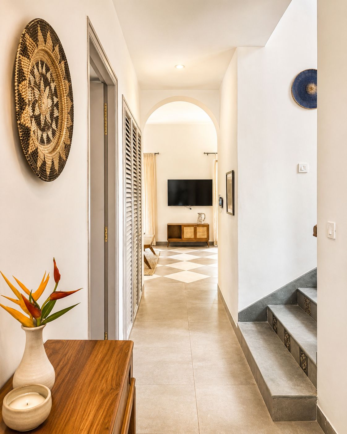 Un pasillo con una mesa de madera, un florero con flores, un televisor montado en la pared y una escalera.