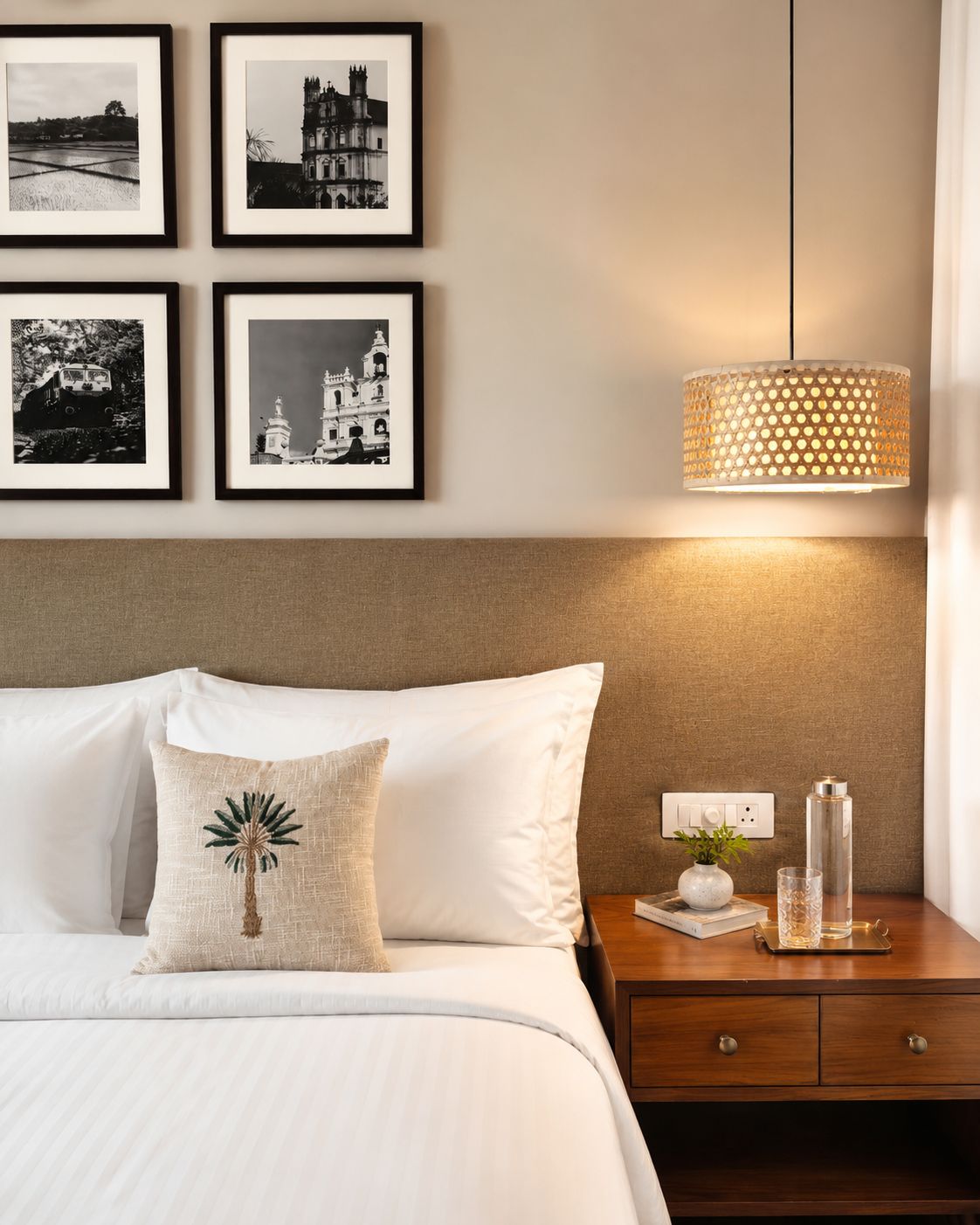 Una habitación de hotel con una cama bien hecha, una mesita de noche con una lámpara y cuatro cuadros en la pared.