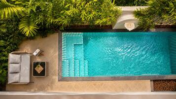A rooftop pool with a tiled edge, surrounded by lush greenery and a seating area with a towel and a small table.