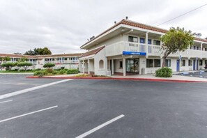 Um motel com uma placa de 'Welcome', estacionamento e um edifício com telhado de telhas vermelhas.