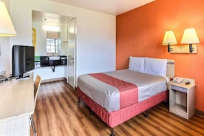 A hotel room with a bed, bedside table, lamp, and a desk with a chair.
