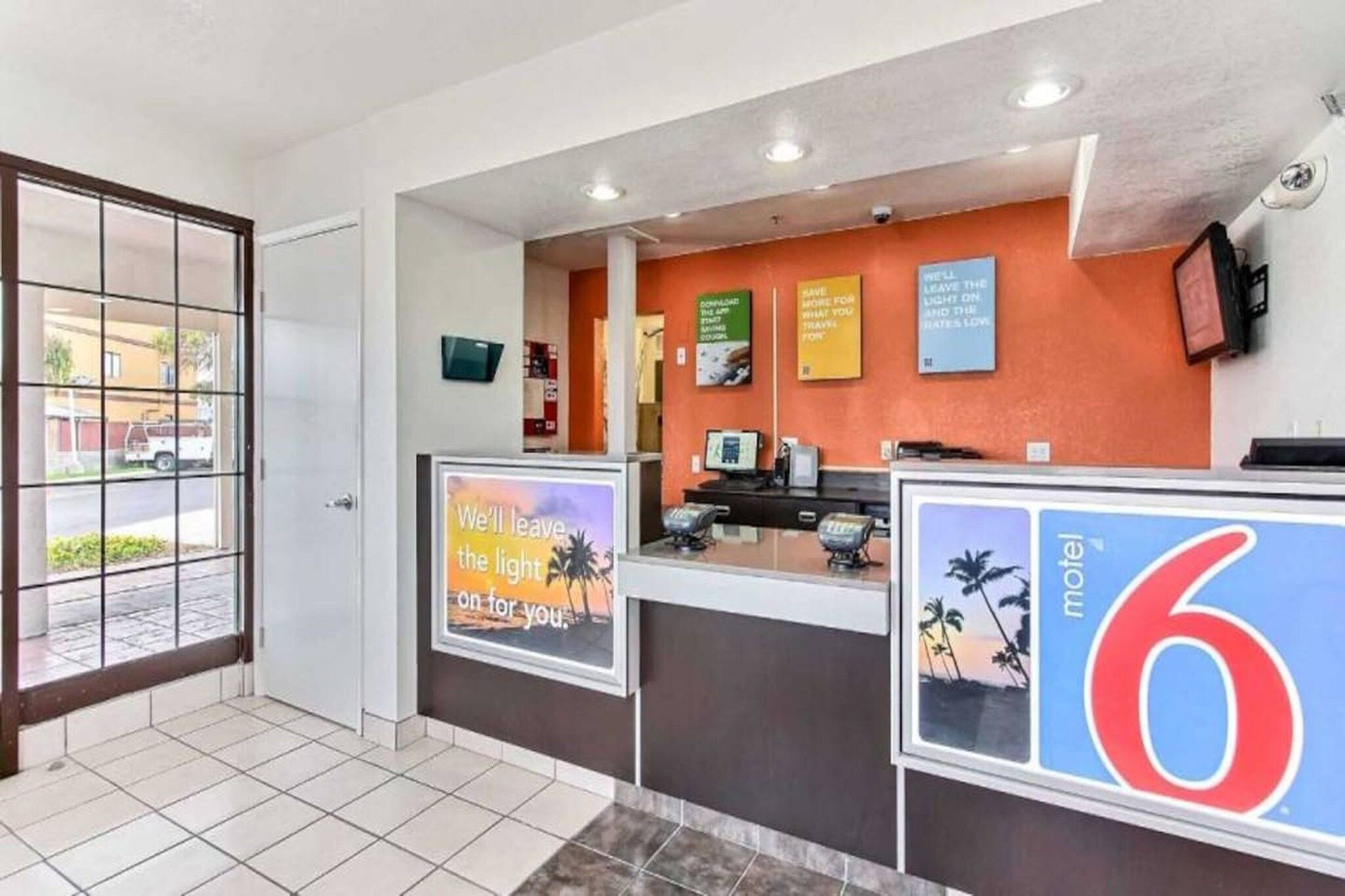 A hotel reception area with a tiled floor, a reception desk, a computer, and a large sign indicating room number 6.