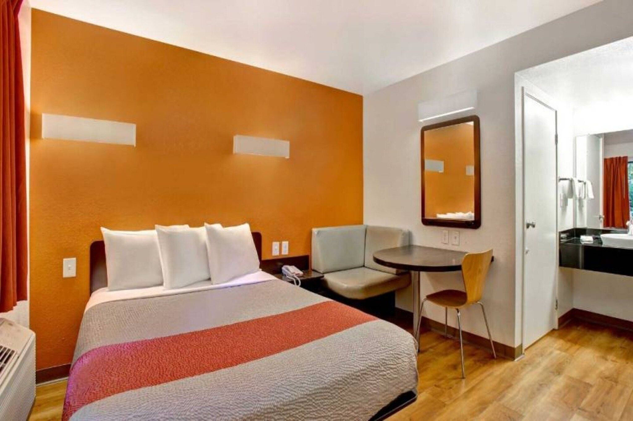 Habitación de hotel con cama, escritorio, silla, espejo y baño.