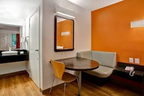 Habitación de hotel con una mesa redonda, una silla, un sofá, un espejo y un teléfono.