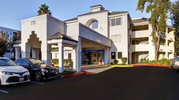 A hotel with a modern facade, a prominent entrance, and a parking lot with several cars.