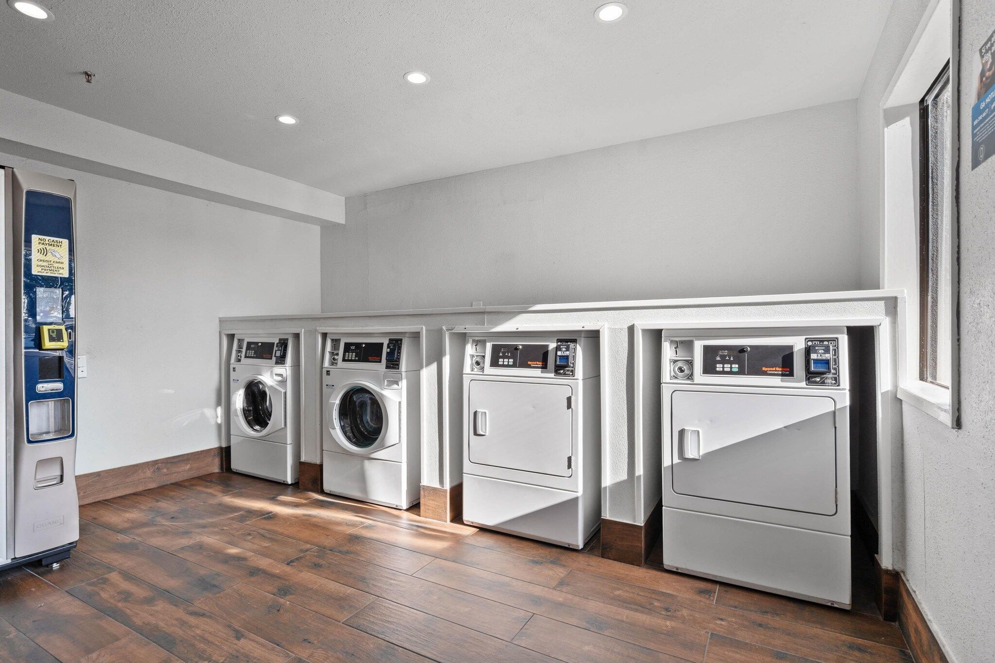 A laundry room with four washing machines, a payment terminal, and a wooden floor.