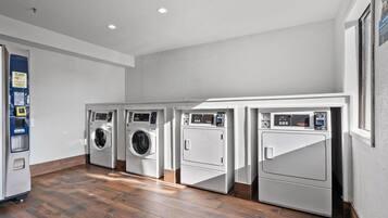 A laundry room with four washing machines, a payment terminal, and a wooden floor.