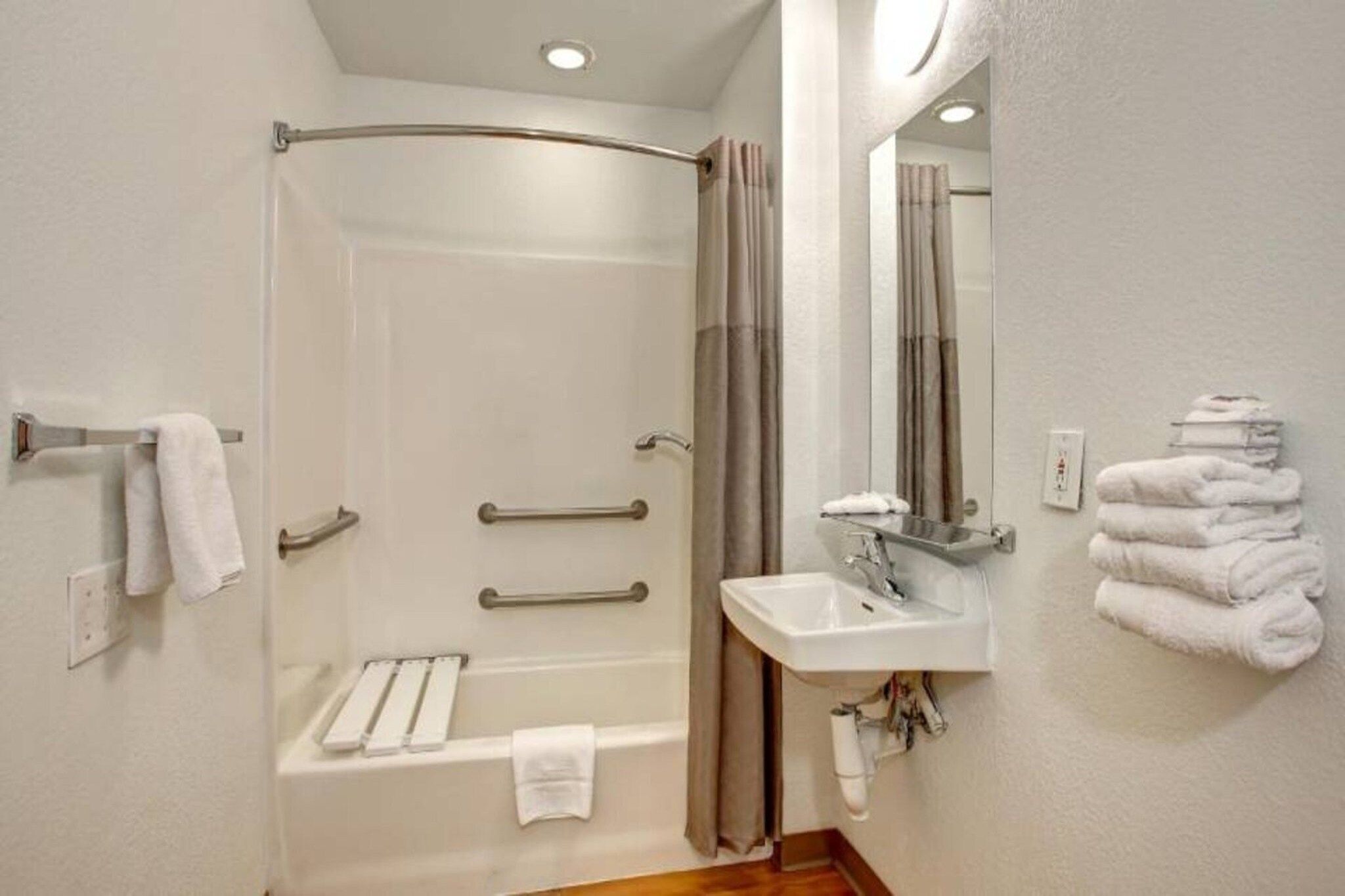 A bathroom with a shower, a sink, and a mirror. There are towels and a towel rack.