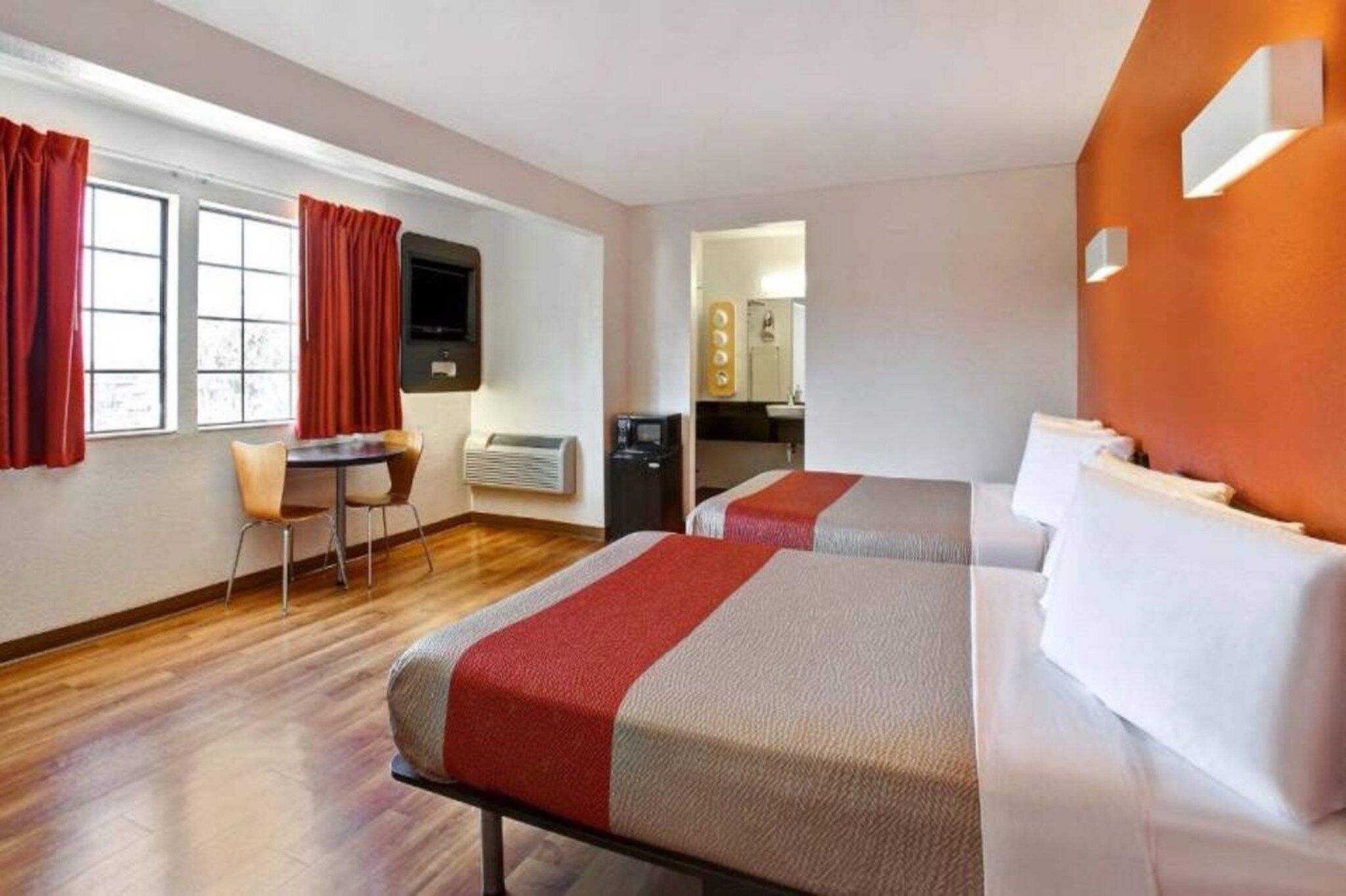 A hotel room with two beds, a desk, and a kitchenette.