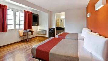 A hotel room with two beds, a desk, and a kitchenette.