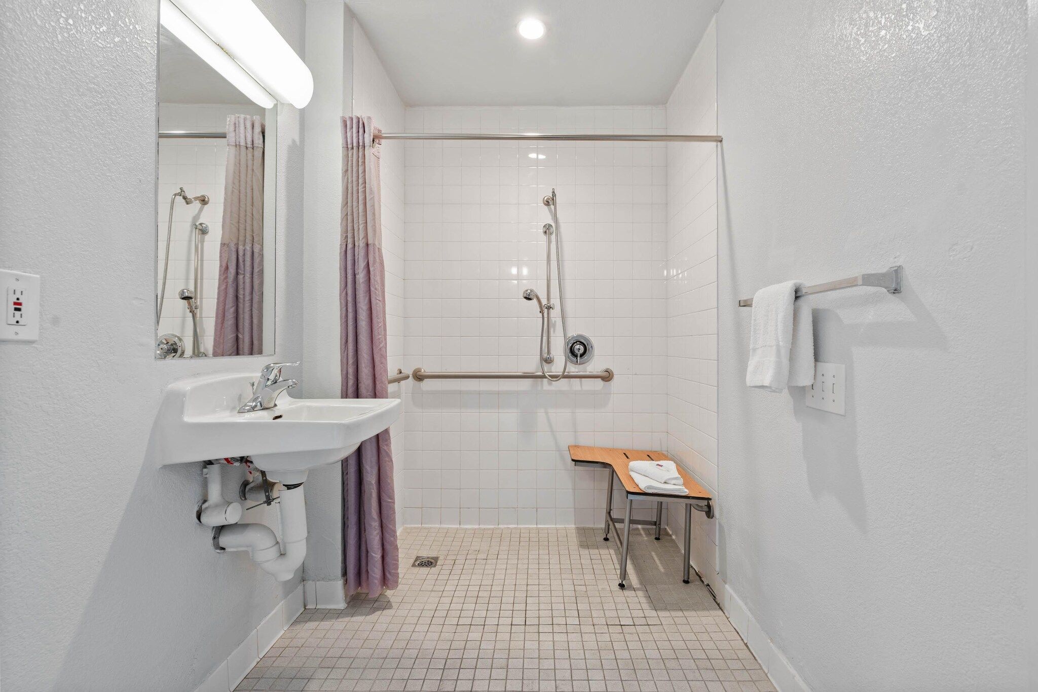 A bathroom with a shower, a sink, a mirror, and a bench.