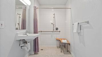 A bathroom with a shower, a sink, a mirror, and a bench.