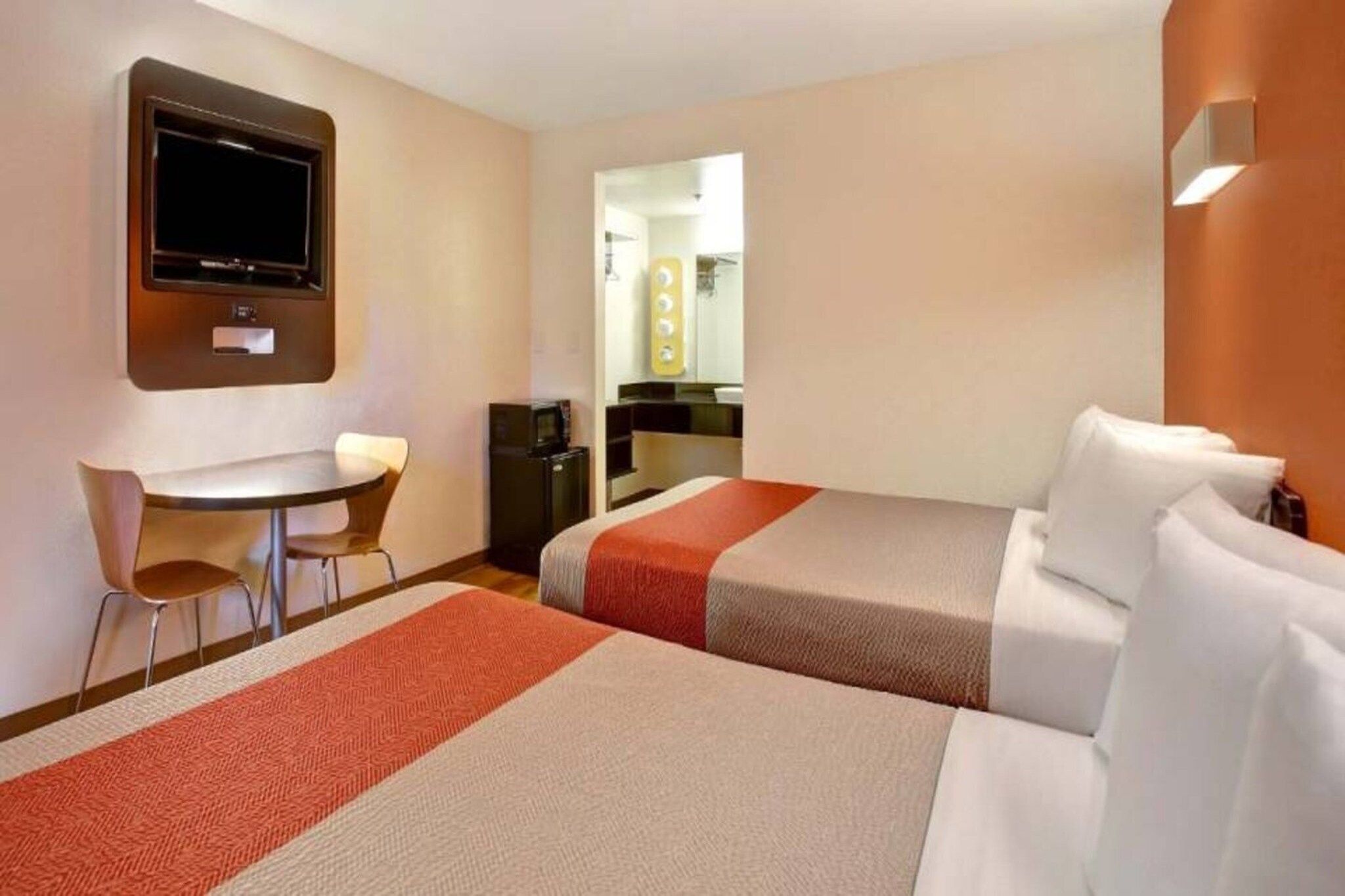 A hotel room with two beds, a desk, a chair, a television, and a bathroom visible through an open door.