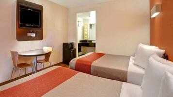 A hotel room with two beds, a desk, a chair, a television, and a bathroom visible through an open door.