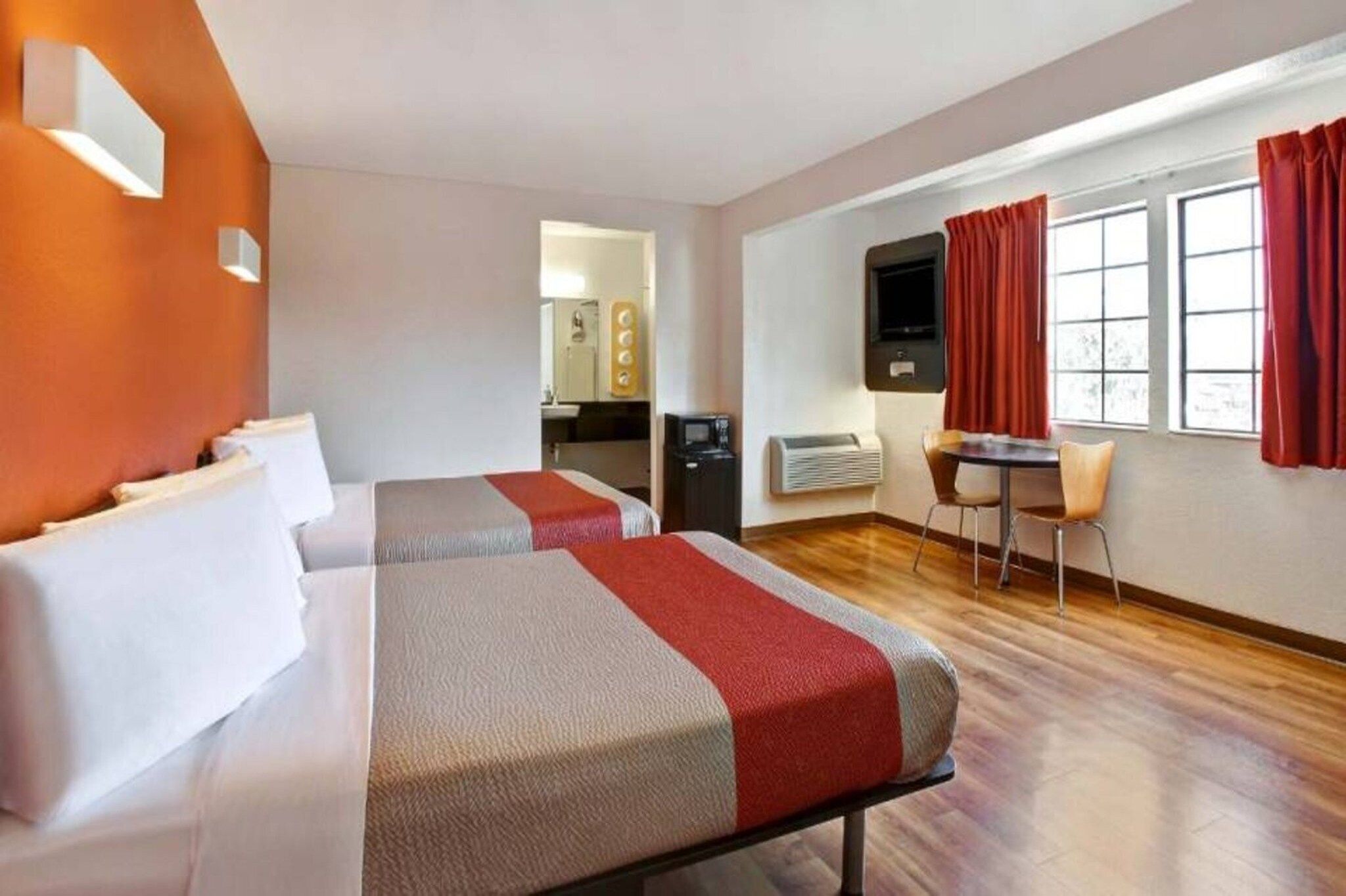 A hotel room with two beds, a desk, a chair, a TV, and a window with curtains.