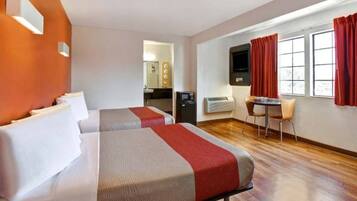 A hotel room with two beds, a desk, a chair, a TV, and a window with curtains.